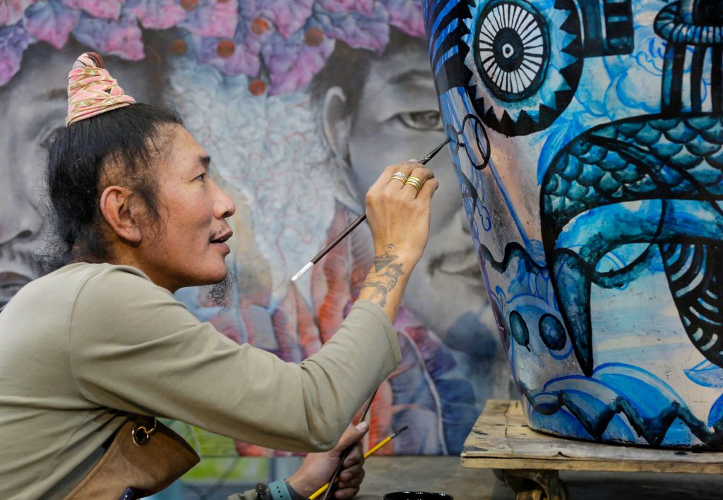 Họa sĩ đang vẽ một tác phẩm nghệ thuật phức tạp với màu xanh lam trên bề mặt cong