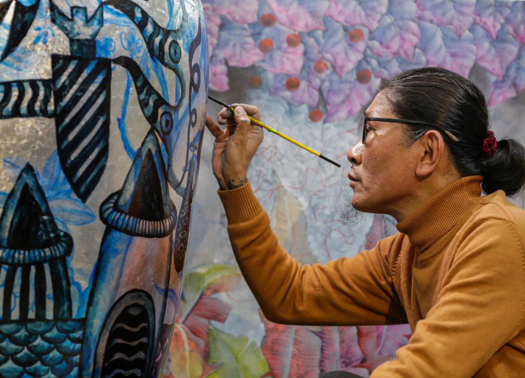 Họa sĩ đang vẽ một tác phẩm nghệ thuật lớn với màu sắc tươi sáng và độc đáo