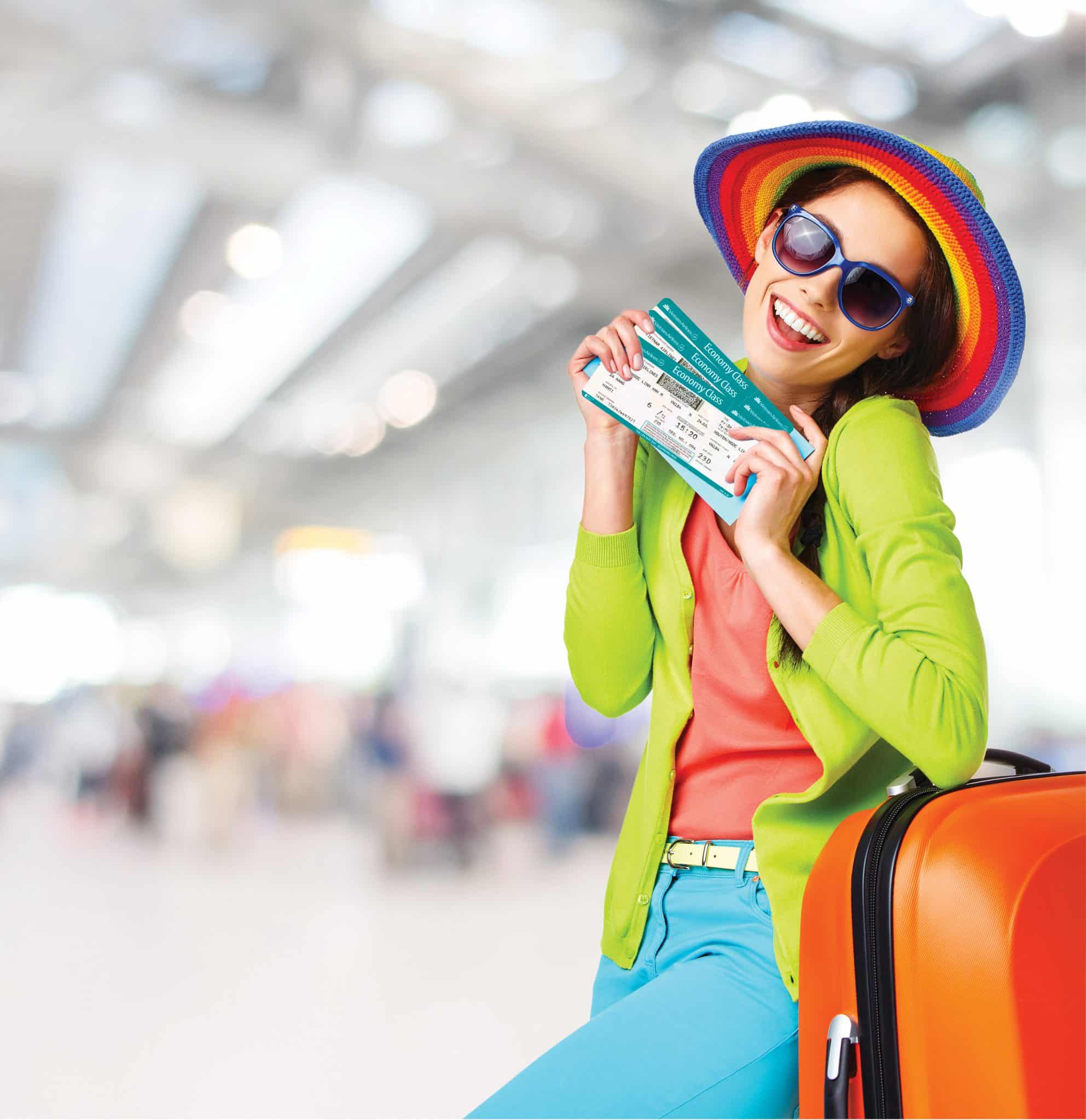 A smiling woman holds airline tickets and stands with orange luggage