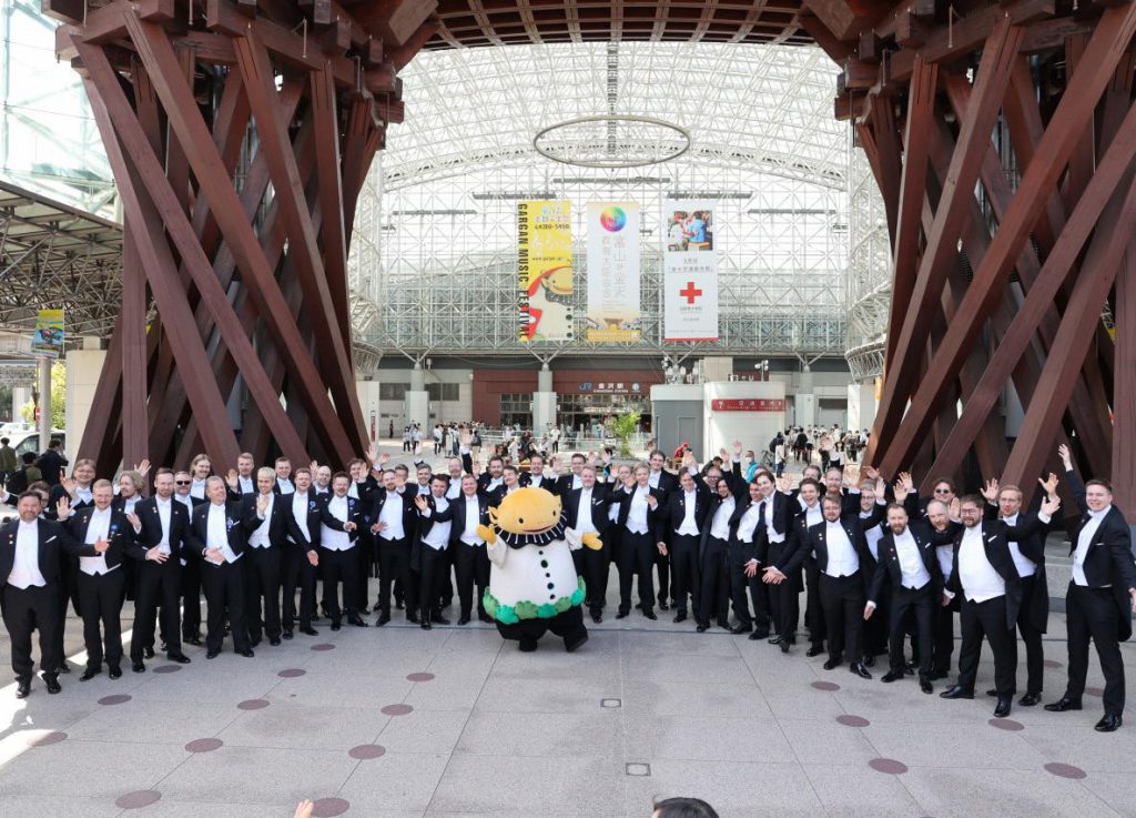 D&agrave;n nhạc giao hưởng mặc vest lịch sự chụp ảnh tập thể với ch&uacute; chim c&aacute;nh cụt đ&aacute;ng y&ecirc;u ngo&agrave;i trời